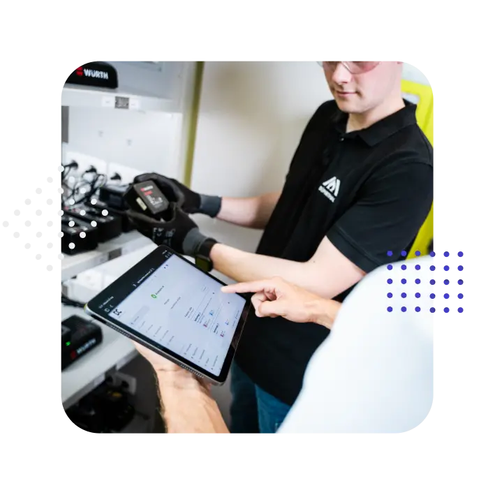 Zwei Personen arbeiten mit einem Tablet und einem technischen Gerät in einem industriellen Umfeld.