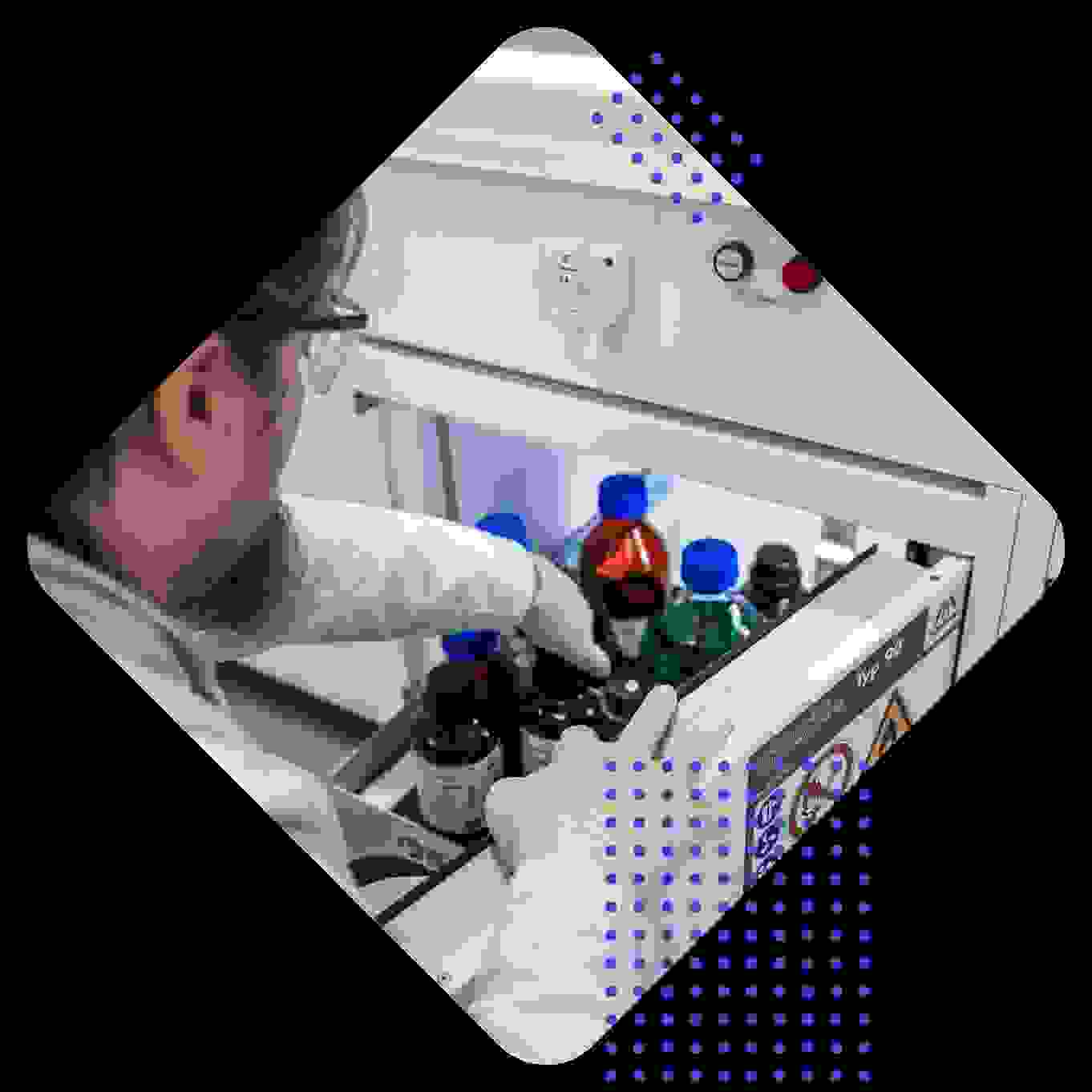 Eine Person im Labor trägt Handschuhe und greift in eine Schublade mit farbigen Flaschen und Chemikalien.