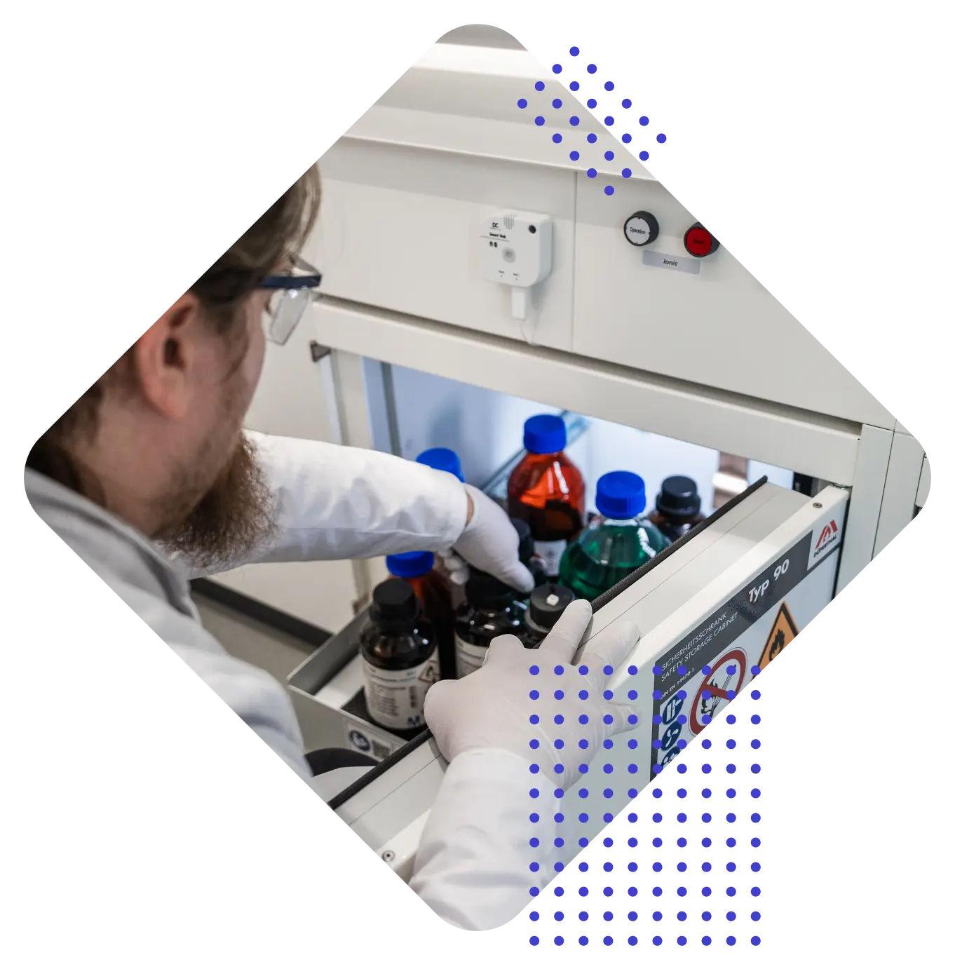 Eine Person im Labor trägt Handschuhe und greift in eine Schublade mit farbigen Flaschen und Chemikalien.