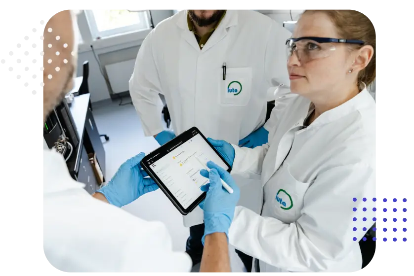 Drei Personen in Laborkitteln schauen auf ein Tablet und diskutieren.