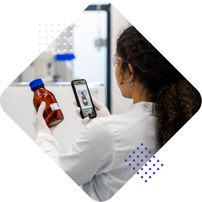Eine Person in einem Labor hält eine braune Flasche mit Blauen Deckel in der einen Hand und ein Smartphone in der anderen Hand, auf dem sie Informationen anzeigt.
