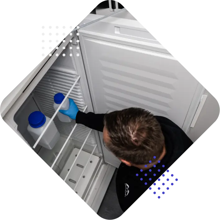 A person wearing blue gloves is reaching into a fridge to grab a container with a blue lid.