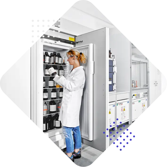 A woman in a lab coat organizes bottles in a storage refrigerator within a laboratory setting.