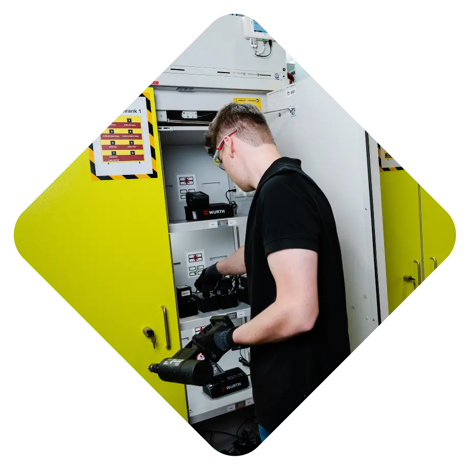 A person in a black shirt is organizing equipment in a yellow cabinet with several shelves, where tools and accessories are stored.