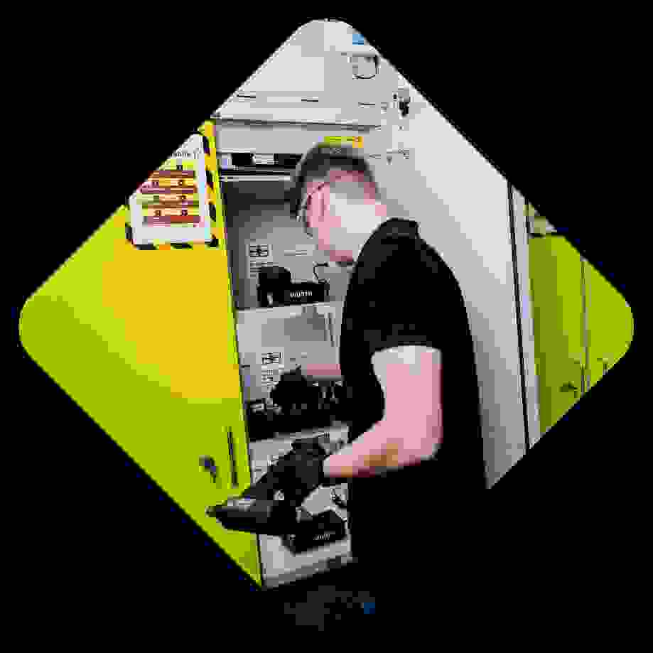 A person in a black shirt is organizing equipment in a yellow cabinet with several shelves, where tools and accessories are stored.