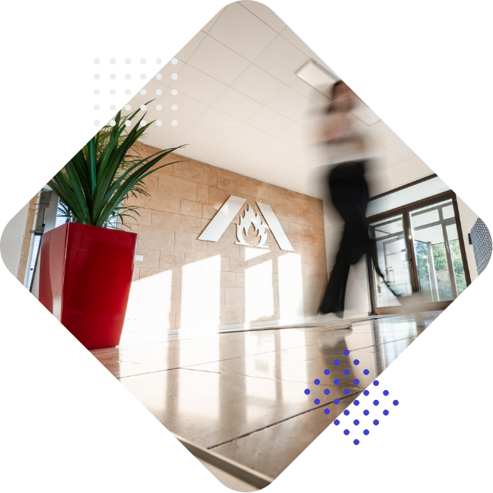 A blurred figure walks past a large logo on a stone wall, with a potted plant in a red planter visible in the foreground.