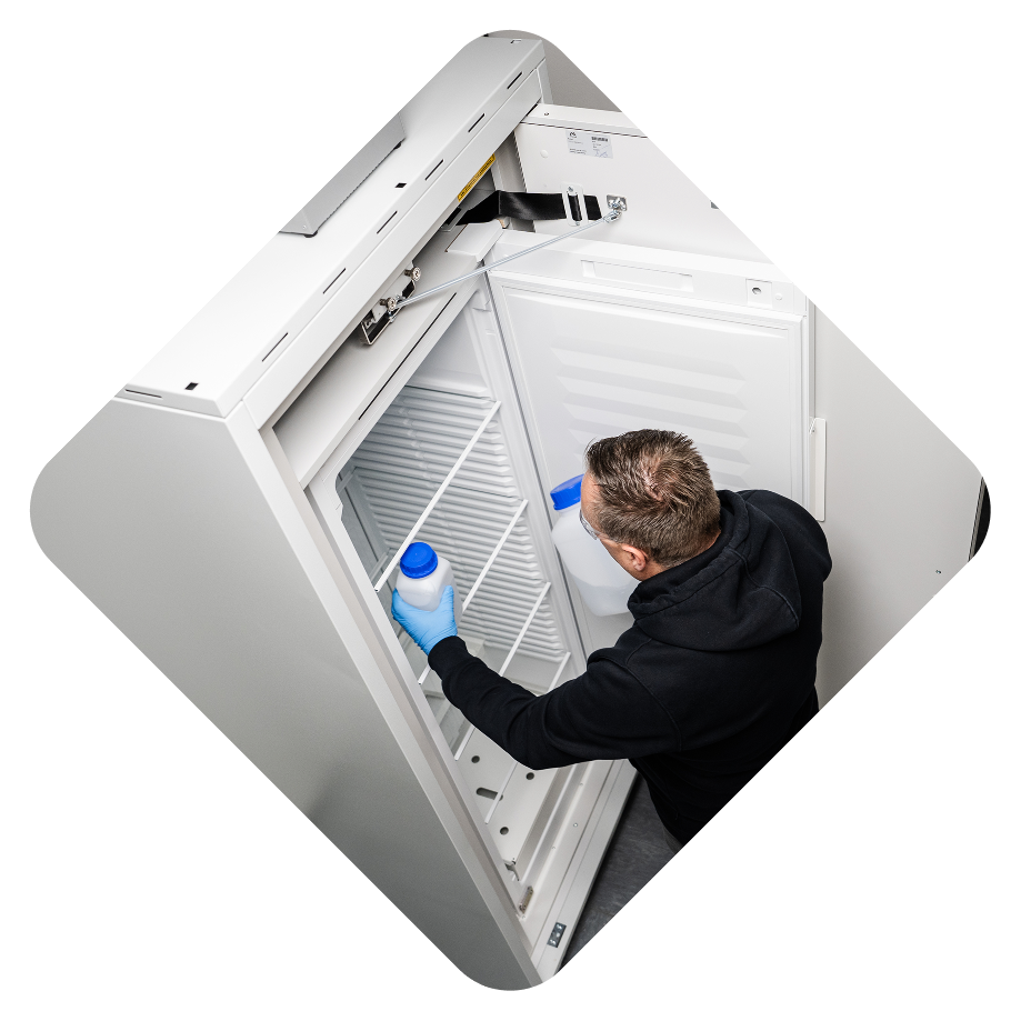 A person cleaning the interior of a white refrigerator, holding a bottle of cleaning solution.