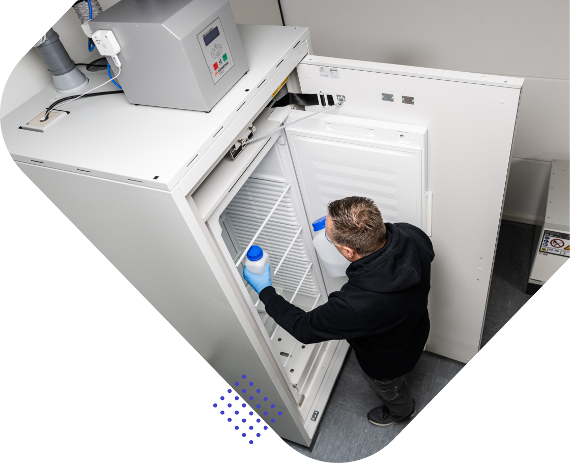 A person in a hoodie and gloves is organizing items inside a large freezer while holding a blue container.