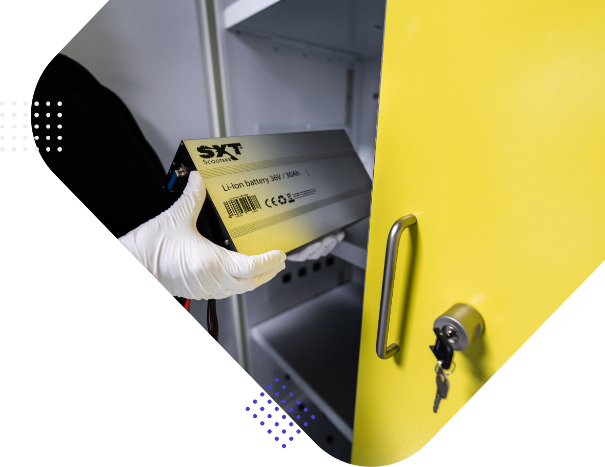 A hand wearing a white glove holds a Li-Ion battery tagged "SXT Scooters" while reaching into a yellow cabinet.