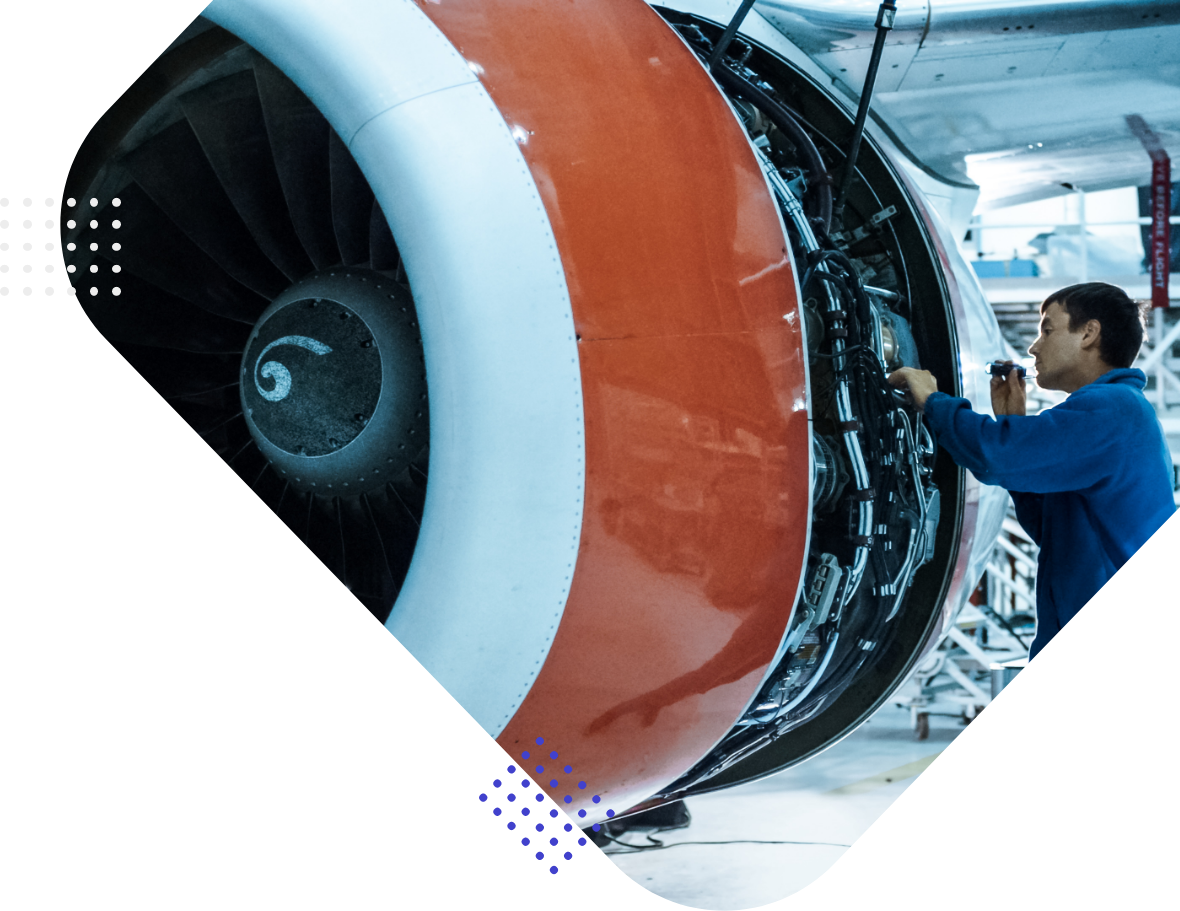 A technician examines the exterior of a jet engine in an aircraft maintenance facility.