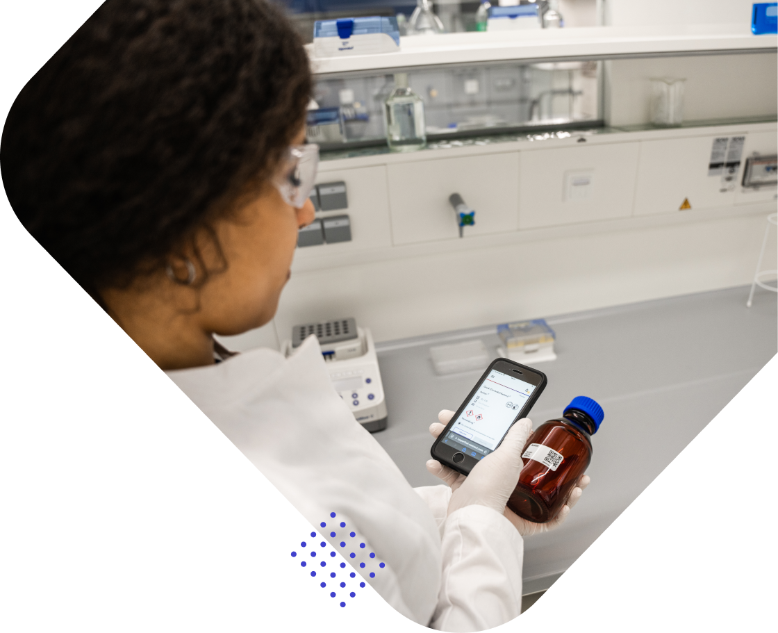 Eine Person in einem Labor, die einen braunen Fläschchen mit blauem Deckel in der Hand hält und ein Smartphone betrachtet.
